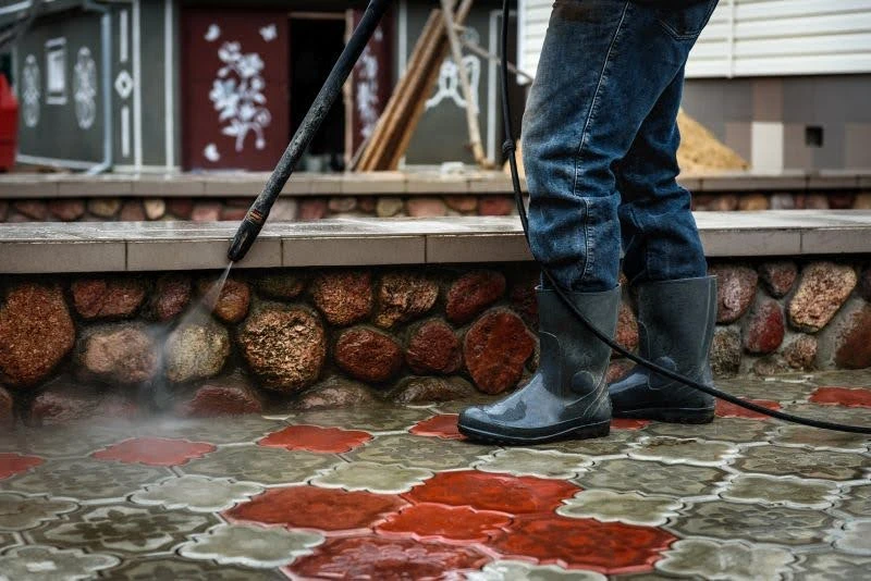 človek v gumákoch čistí zámkovú dlažbu vysokotlakovým čističom