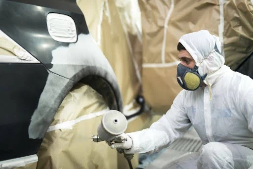 muž v ochrannom odeve sprejuje auto, pričom niektoré časti auta sú dôkladne zakryté